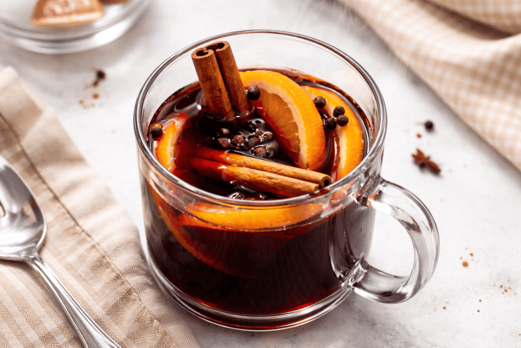 Mulled wine with orange slices, cinnamon, and spices in a glass mug.