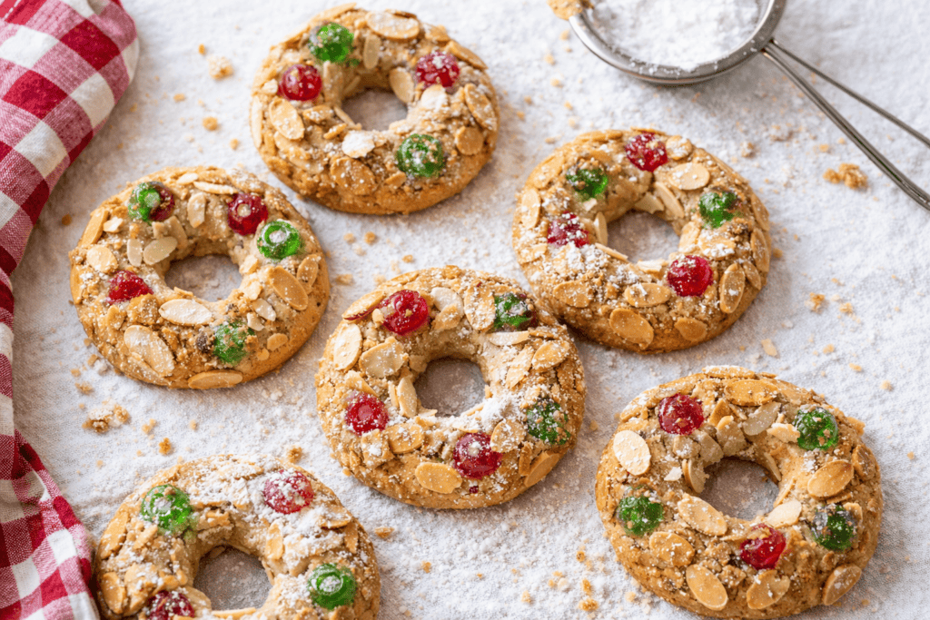 Almond cookies decorated with colorful red and green candies, dusted with powdered sugar, on a bakin.