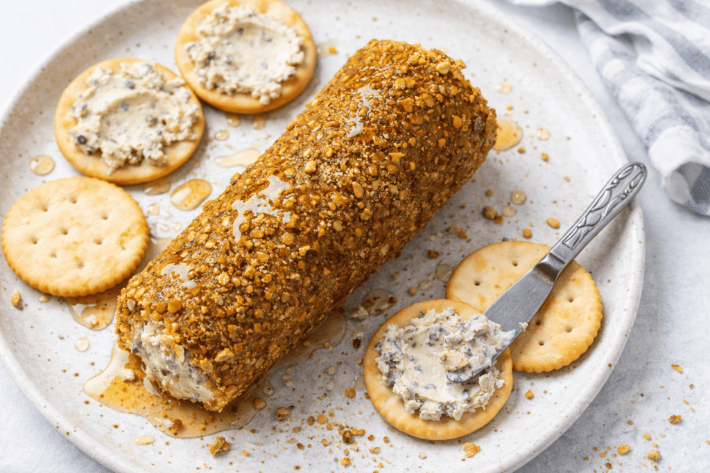 Blue cheese log coated with crushed nuts on a white plate with crackers.