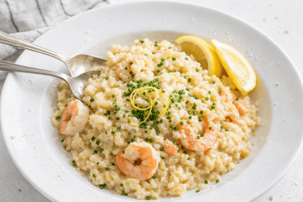 Delicious shrimp risotto with lemon wedges and fresh herbs on a white plate.